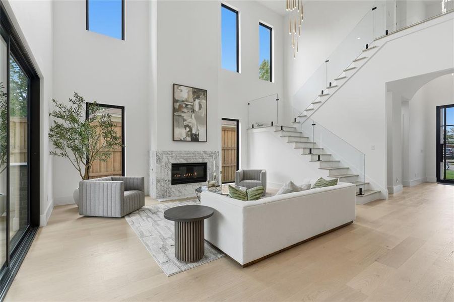 Two-story living area featuring a marble-clad fireplace, light wood-finish flooring, and a contemporary open-riser staircase with glass railing Two-story living area featuring a marble-clad fireplace, light wood-finish flooring, and a contemporary open-riser staircase with glass railing