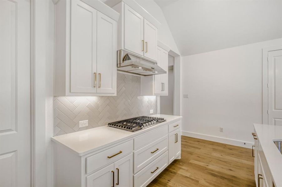 Kitchen featuring white cabinets, vaulted ceiling, light wood-type flooring, stainless steel gas stovetop, and light stone countertops