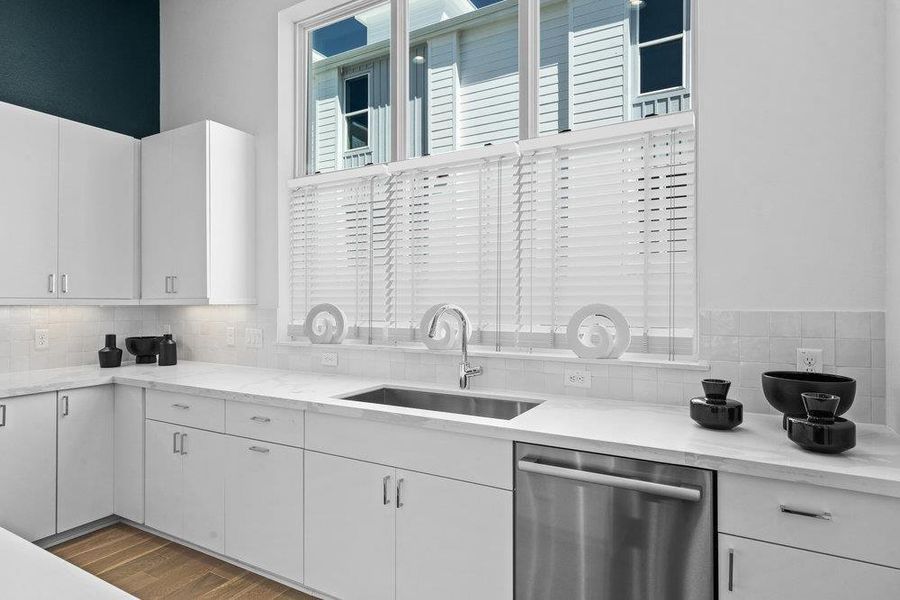 Kitchen with stainless steel dishwasher, white cabinets, wood finished floors, light stone countertops, and decorative backsplash