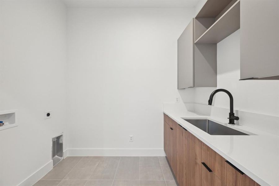 Clothes washing area featuring sink, light tile patterned floors, electric dryer hookup, cabinets, and washer hookup