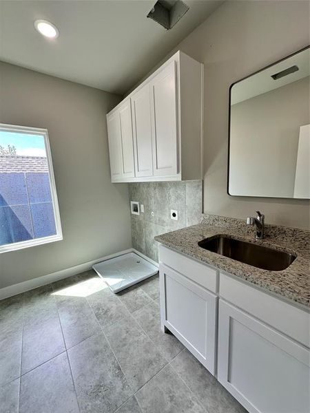 Clothes washing area with light tile floors, electric dryer hookup, washer hookup, and sink