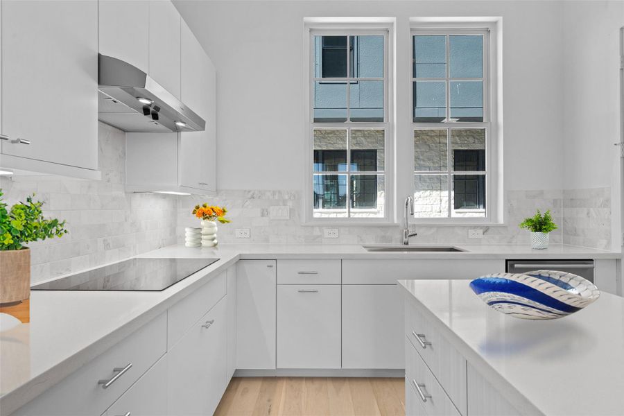 Kitchen featuring white cabinets, under cabinet range hood, light wood-style flooring, black electric cooktop, and backsplash