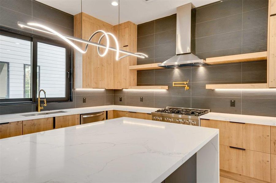 Kitchen featuring sink, wall chimney range hood, light stone counters, backsplash, and decorative light fixtures