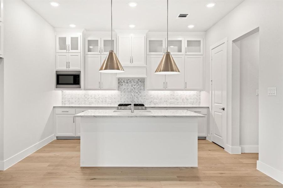 Kitchen with built in microwave, light hardwood / wood-style flooring, white cabinetry, hanging light fixtures, and an island with sink