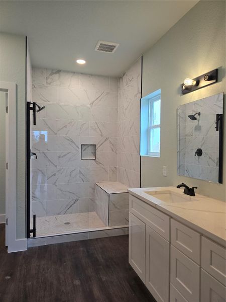 Bathroom featuring vanity, a marble finish shower, and dark wood-style flooring