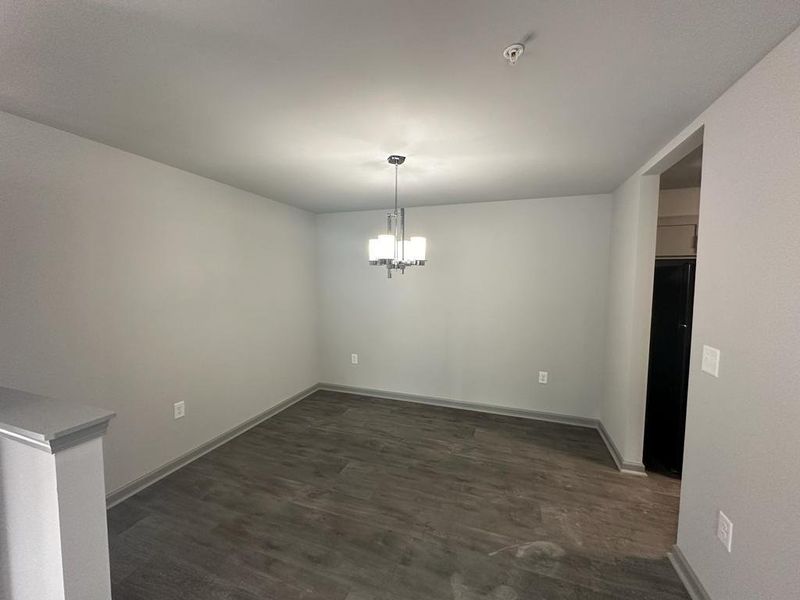 Empty room with dark hardwood / wood-style flooring and a notable chandelier