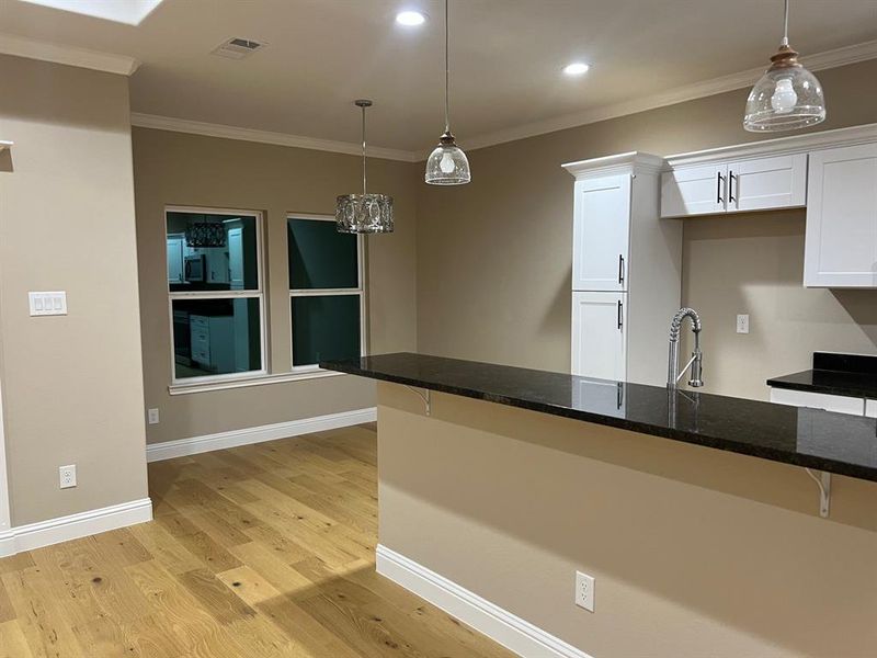 Kitchen with pendant lighting, dark stone counters, white cabinetry, light hardwood / wood-style flooring, and ornamental molding