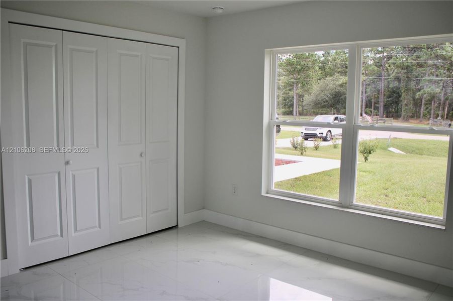 Room with polished tile flooring, white interior finishes, multi-panel closet doors, and large dual-pane windows