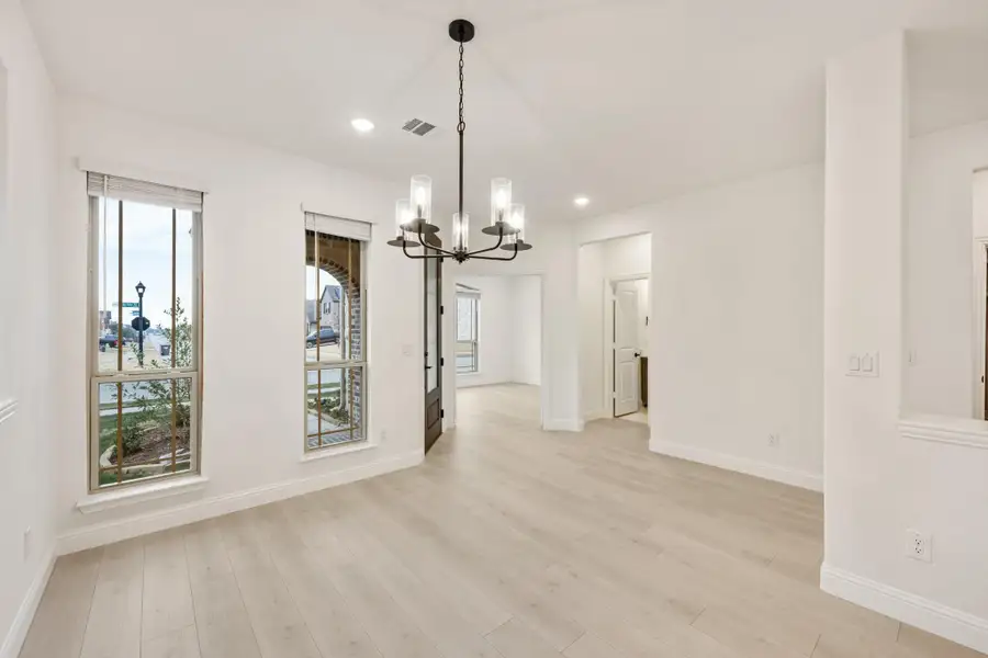 Open dining area with light wood floors, white walls, and a black chandelier overhead Open dining area with light wood floors, white walls, and a black chandelier overhead