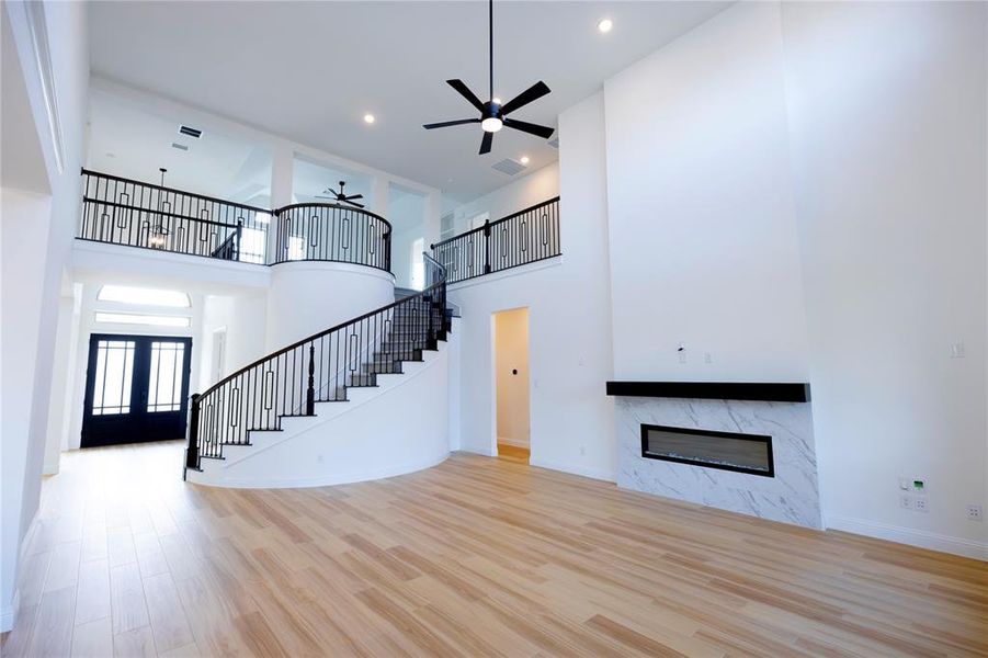 Unfurnished living room featuring french doors, a high end fireplace, light hardwood / wood-style flooring, and a high ceiling