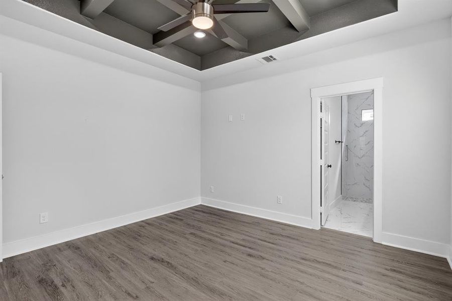 Room featuring wood-finish flooring, a tray ceiling with exposed beams, and a modern ceiling fan
