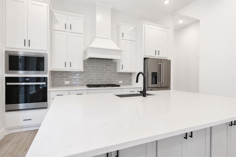 Kitchen featuring an expansive island with a matte black faucet, white shaker cabinetry, stainless steel appliances, and a gray subway tile backsplash