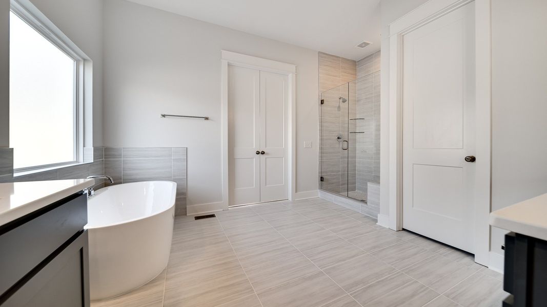 Large tiled bathroom with multiple vanities, glass shower enclosure, and freestanding tub