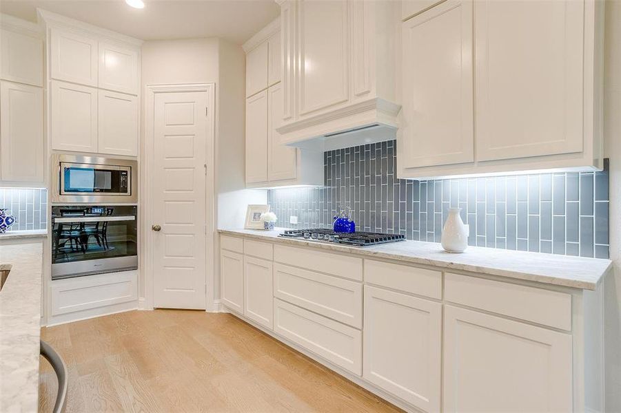 Kitchen with light stone counters, tasteful backsplash, white cabinetry, stainless steel appliances, and light wood-type flooring