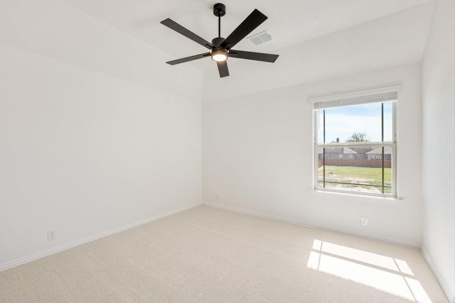 Empty bedroom with beige carpet, white walls, black ceiling fan, and a window with backyard view