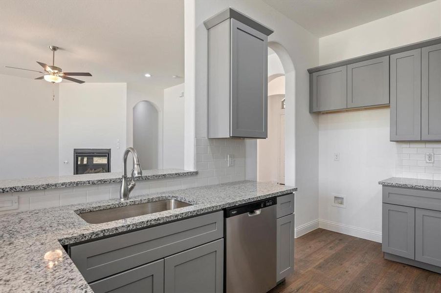 Kitchen with gray cabinets, tasteful backsplash, stainless steel dishwasher, and light stone counters