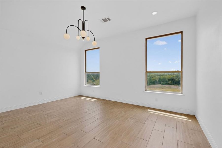 Spacious room featuring wood-finish tile flooring, two large windows with natural light, a contemporary chandelier, recessed lighting, and white baseboards Spacious room featuring wood-finish tile flooring, two large windows with natural light, a contemporary chandelier, recessed lighting, and white baseboards