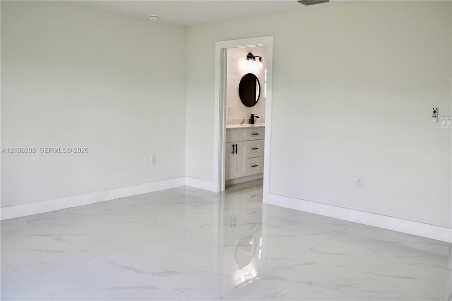 Large-format tile flooring with a stone-finish pattern, paired with a vanity featuring a light-toned countertop, undermount sink, circular wall mirror, and matte black hardware