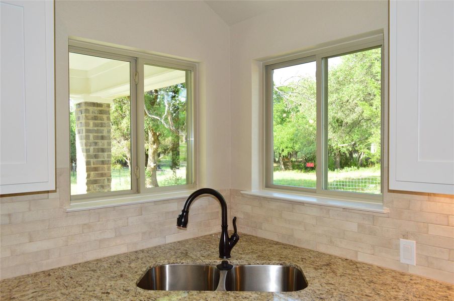 Kitchen featuring decorative backsplash, white cabinets, light stone counters, and vaulted ceiling