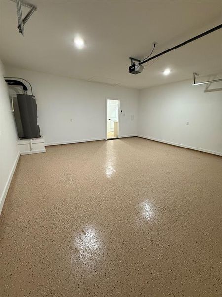 Garage featuring baseboards, a garage door opener, and water heater