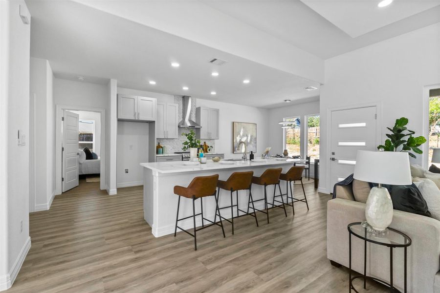 Kitchen featuring open floor plan, a kitchen bar, recessed lighting, light wood finished floors, and a kitchen island with sink