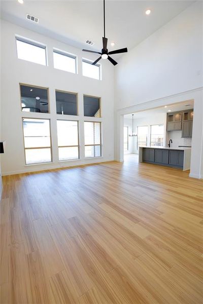 Unfurnished living room with recessed lighting, light wood-type flooring, a towering ceiling, ceiling fan, and a chandelier Unfurnished living room with recessed lighting, light wood-type flooring, a towering ceiling, ceiling fan, and a chandelier