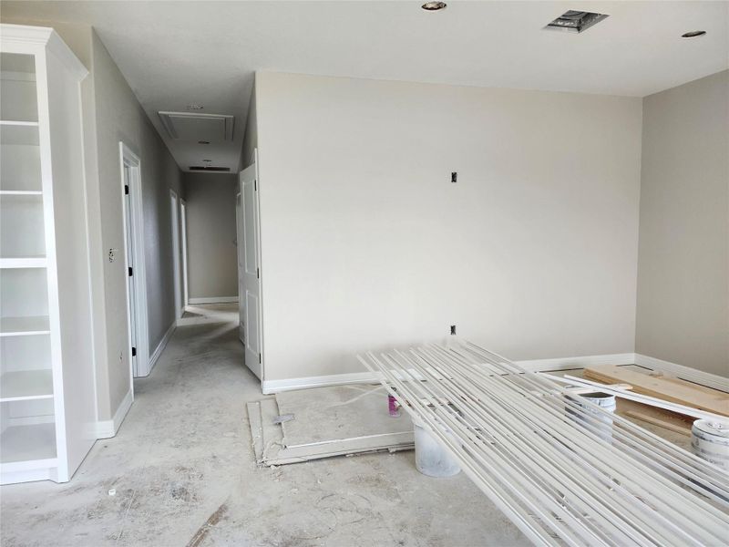 This photo shows a living room with neutral walls and a hallway leading to multiple doors.