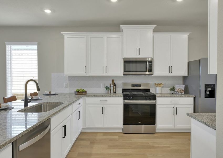 Kitchen featuring an undermount sink beneath a window, granite countertops, white cabinetry, and stainless appliances.