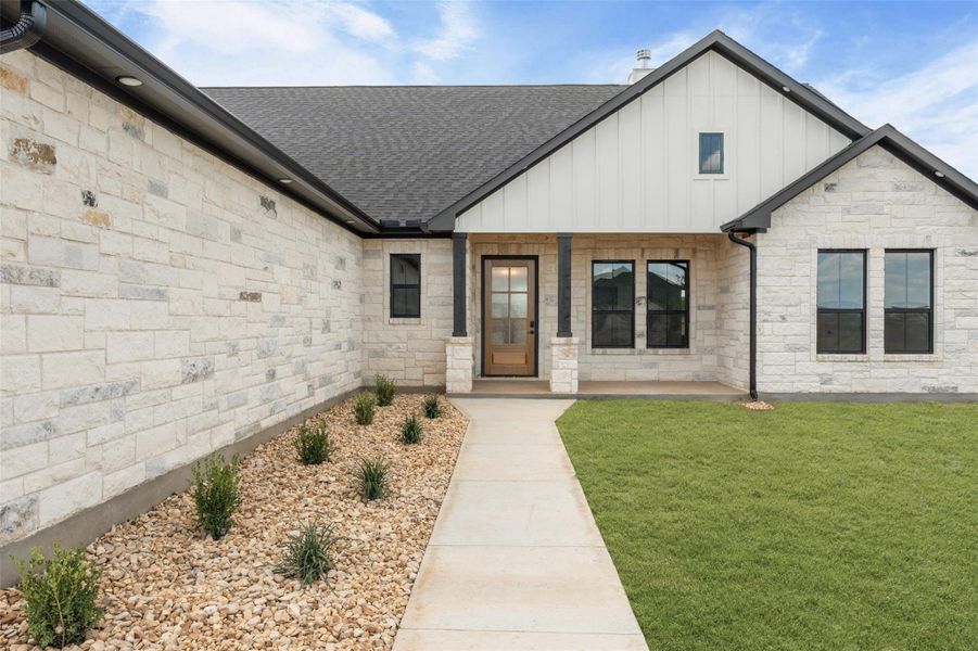 View of front of property with board and batten siding, a porch, stone siding, a front yard, and a shingled roof View of front of property with board and batten siding, a porch, stone siding, a front yard, and a shingled roof