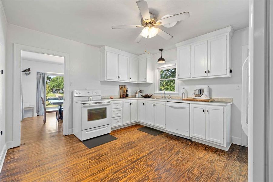 Kitchen featuring white appliances, white cabinetry, decorative light fixtures, and light countertops Kitchen featuring white appliances, white cabinetry, decorative light fixtures, and light countertops