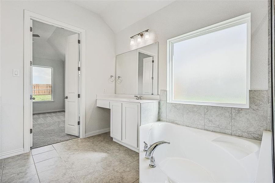 Bathroom featuring vanity, a tub to relax in, tile patterned floors, and vaulted ceiling