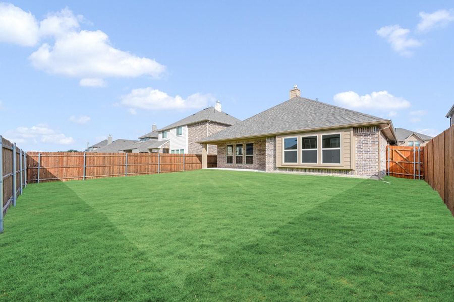 Brick home rear exterior with large grassy backyard enclosed by wood privacy fence