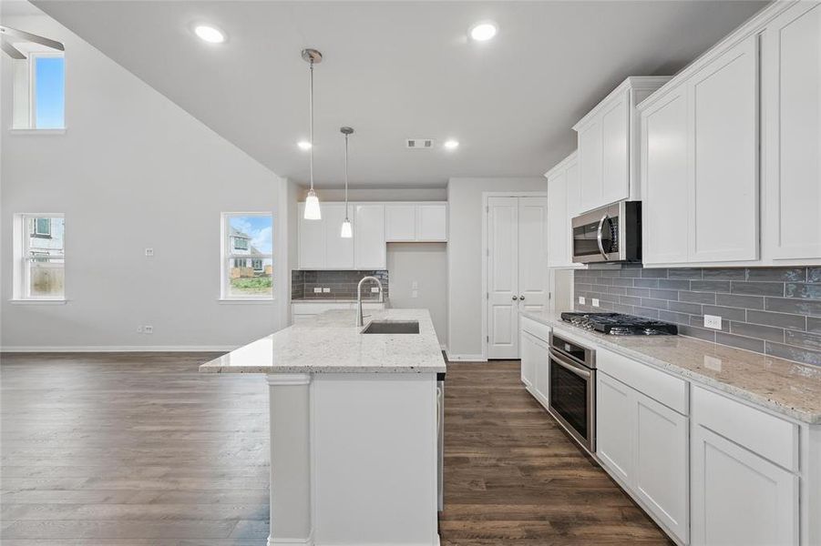 Kitchen featuring decorative light fixtures, light stone counters, a kitchen island with sink, white cabinets, and stainless steel appliances