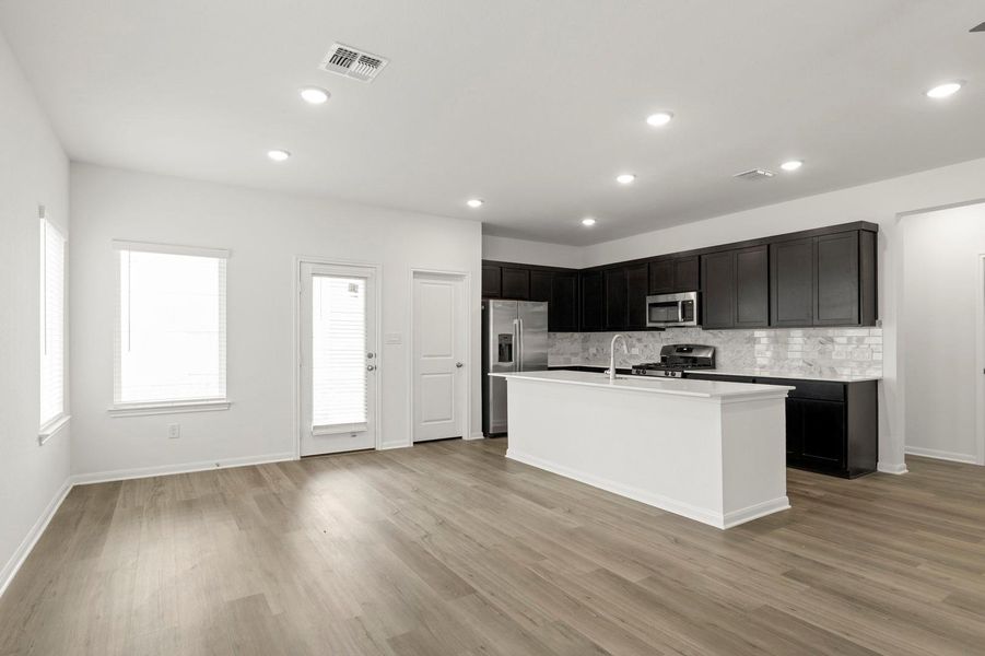 Kitchen featuring dark cabinets, an island with sink, appliances with stainless steel finishes, recessed lighting, and decorative backsplash