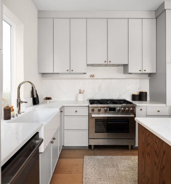 Kitchen with stainless steel appliances, tasteful backsplash, light wood-type flooring, light stone countertops, and white cabinets