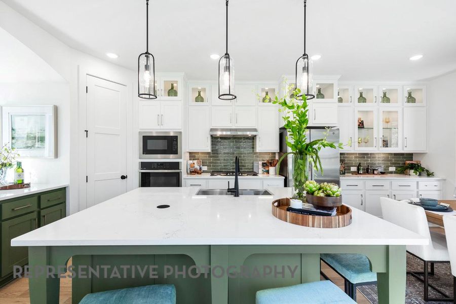 Kitchen with stainless steel appliances, under cabinet range hood, a kitchen breakfast bar, tasteful backsplash, and light countertops Kitchen with stainless steel appliances, under cabinet range hood, a kitchen breakfast bar, tasteful backsplash, and light countertops