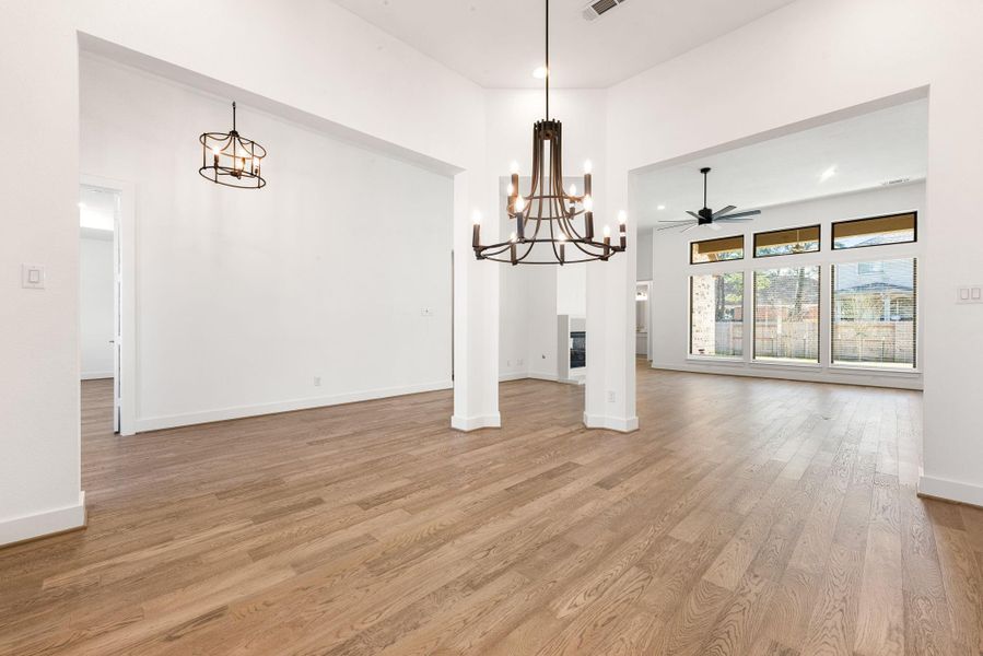 Formal living room open to the family room featuring a gorgeous modern chandelier, large windows, blinds and neutral paint