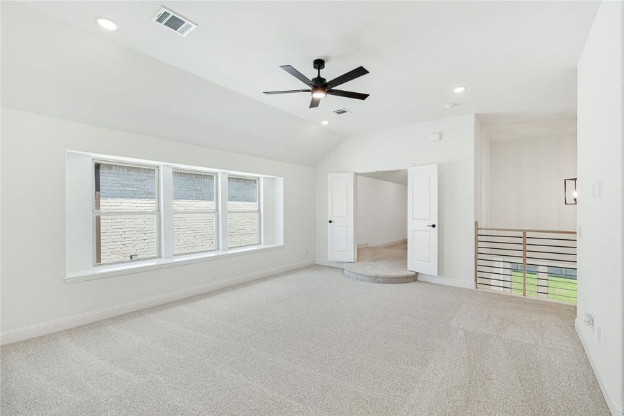 Spacious empty bedroom with vaulted ceiling, ceiling fan, carpet flooring, and open double doors near staircase railing Spacious empty bedroom with vaulted ceiling, ceiling fan, carpet flooring, and open double doors near staircase railing