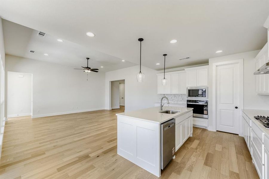 Kitchen with an island with sink, hanging light fixtures, light wood finished floors, open floor plan, and white cabinets