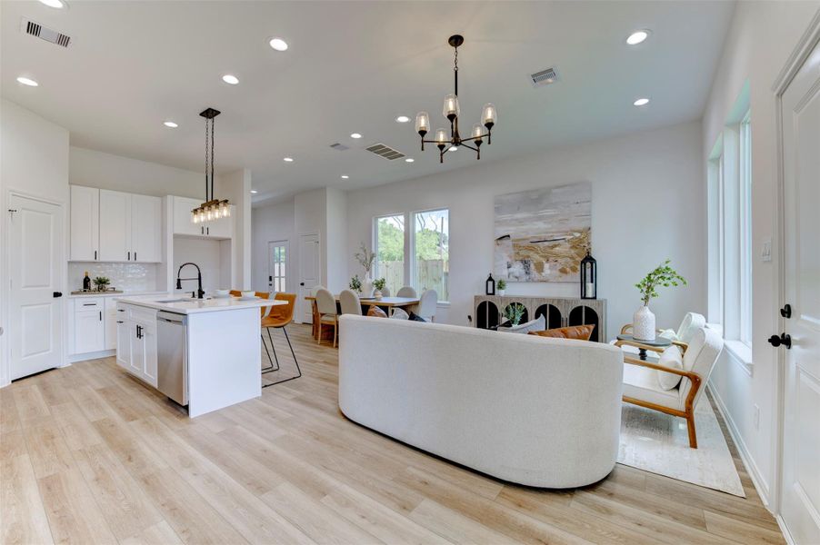 Open-concept first floor with hardwood floors, recessed lighting, two pendant chandeliers, white kitchen with island, dining area, and living room all flowing together. Backyard windows bring in natural light.