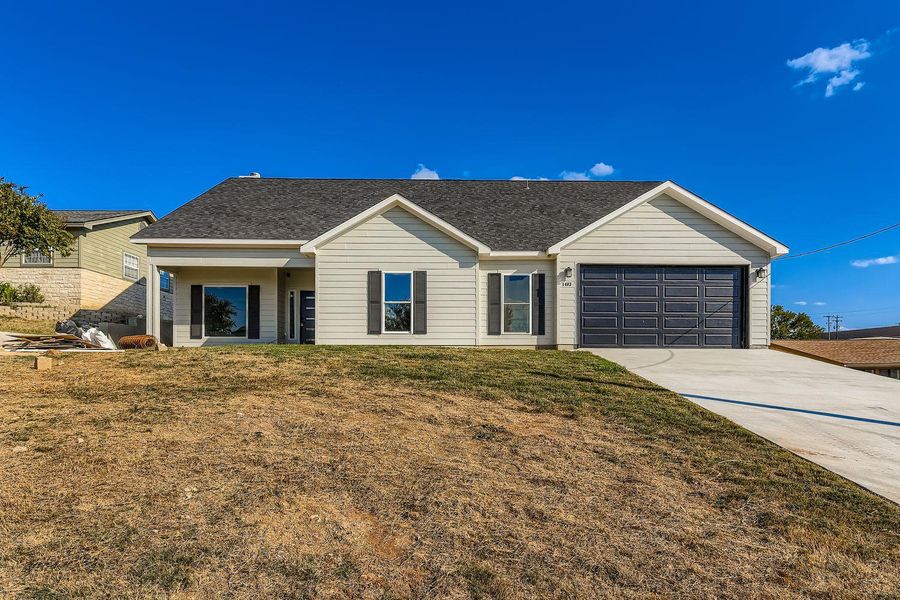 Single story home featuring concrete driveway, a shingled roof, a front lawn, and an attached garage