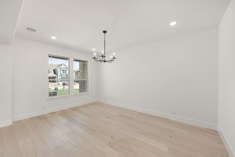 Empty dining room with light hardwood floors, black chandelier, and two windows with neighborhood view