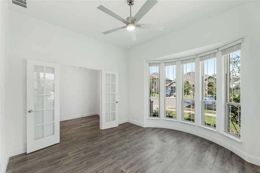 Empty room with hardwood floors, ceiling fan, curved bay window, and French doors Empty room with hardwood floors, ceiling fan, curved bay window, and French doors