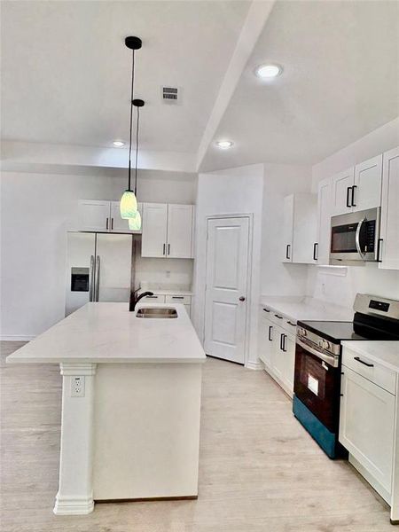 Kitchen featuring appliances with stainless steel finishes, white cabinetry, pendant lighting, an island with sink, and light wood-type flooring