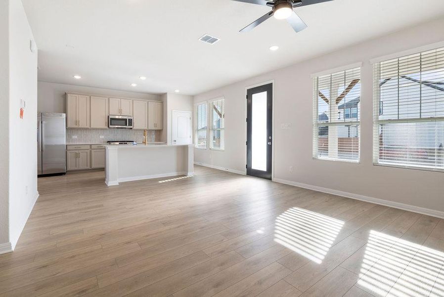 Kitchen featuring stainless steel appliances, a center island with sink, open floor plan, ceiling fan, and light wood-style flooring