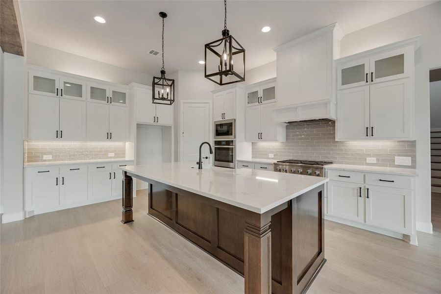 Kitchen featuring glass insert cabinets, backsplash, a kitchen island with sink, white cabinets, and recessed lighting