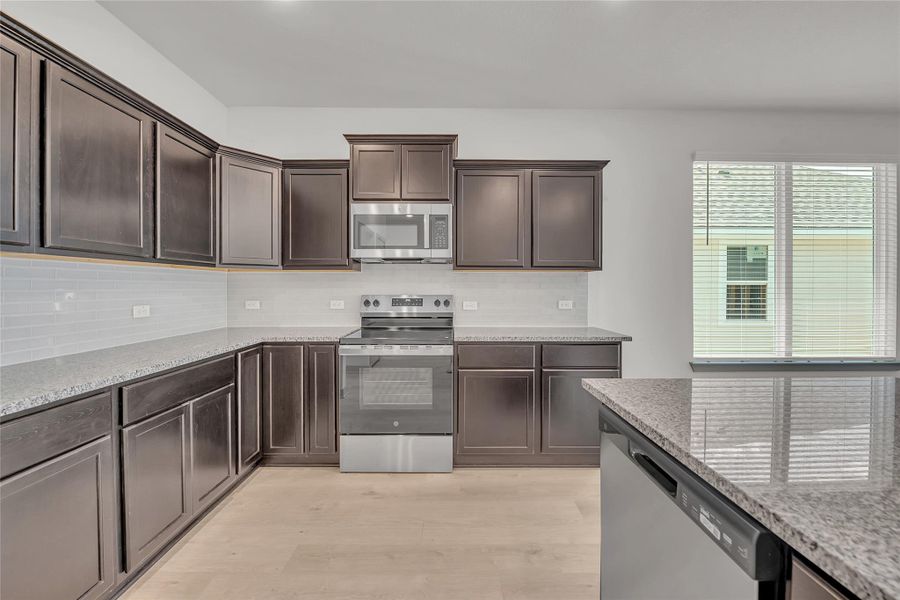 Kitchen featuring stainless steel appliances, dark brown cabinetry, light stone counters, and light wood-type flooring