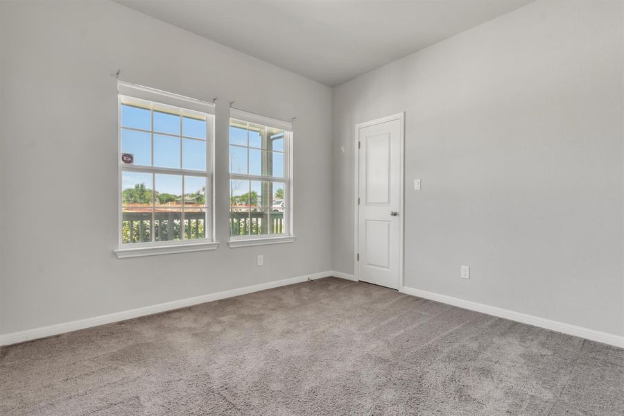A well-lit bedroom features plush carpeting and multiple windows.