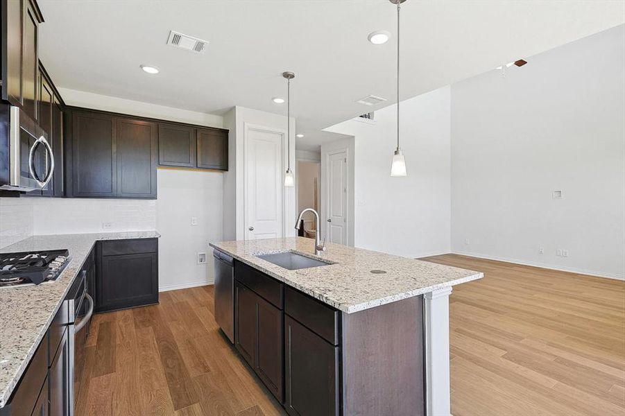 Kitchen featuring decorative light fixtures, stainless steel appliances, sink, light stone countertops, and hardwood / wood-style flooring