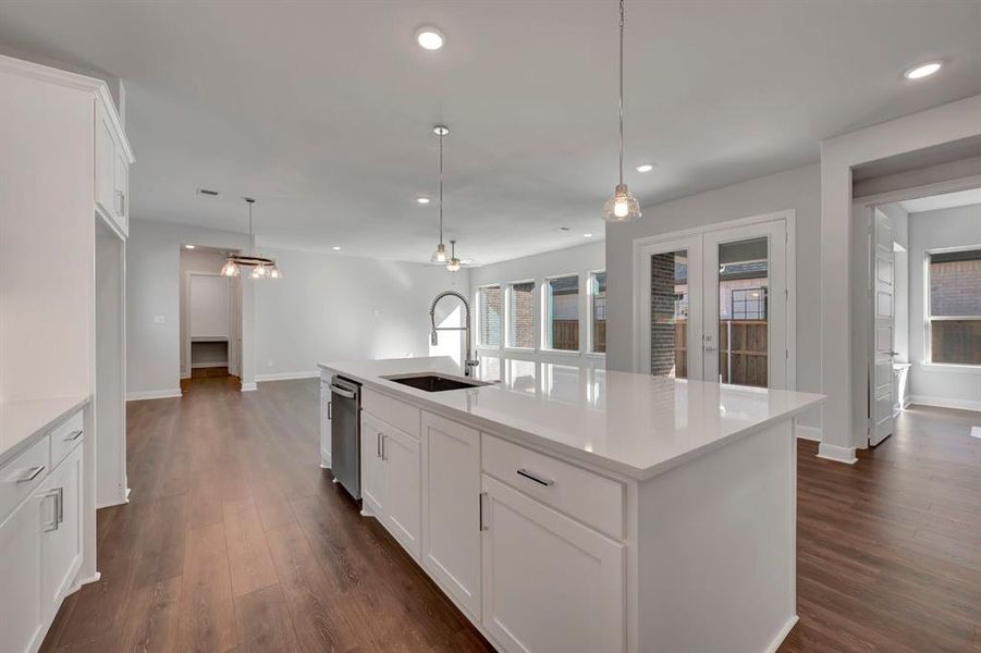 Kitchen with white cabinets, pendant lighting, a center island with sink, and dark wood-style floors